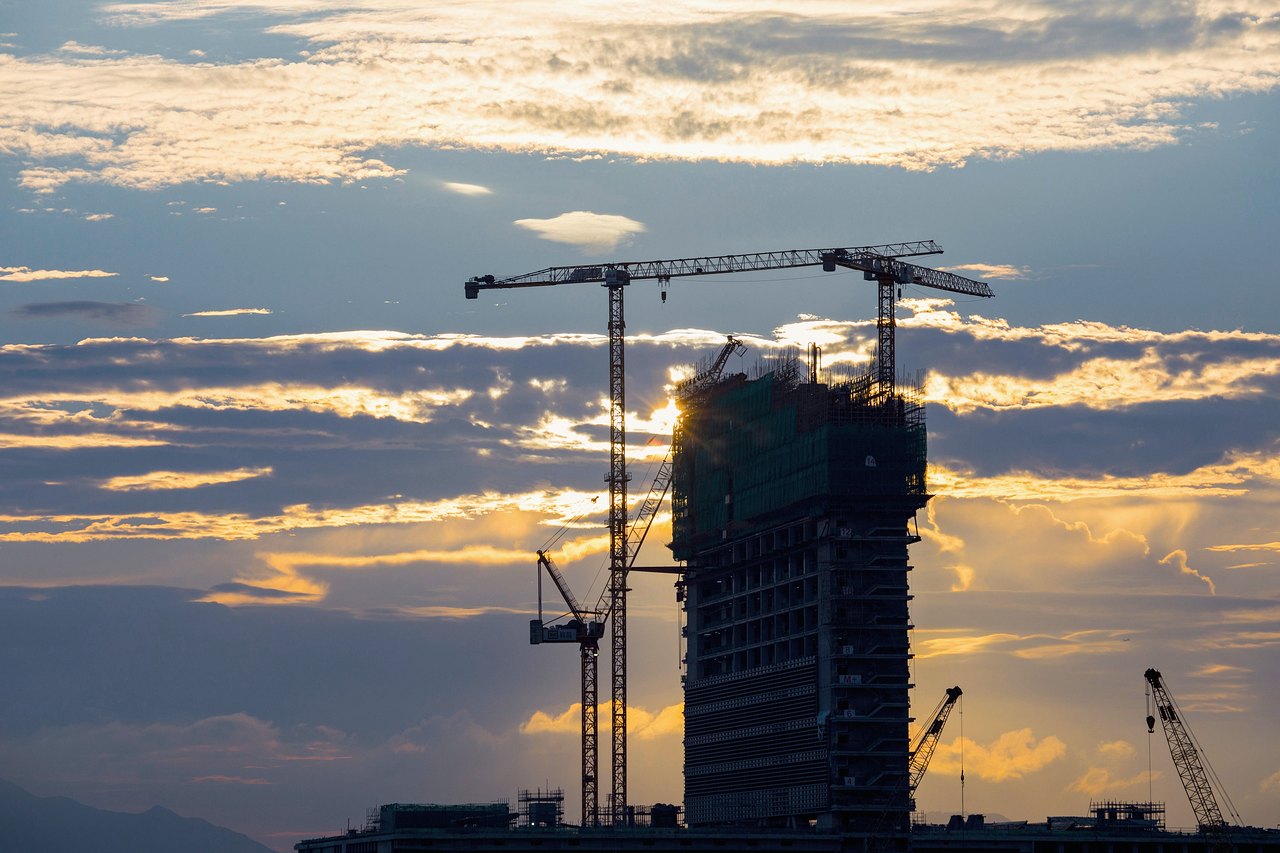 A tower under construction ringed by cranes at dusk