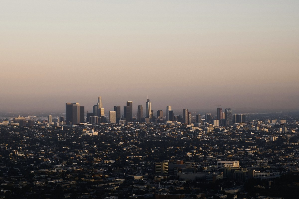 Distant cluster of downtown skyscrapers rising from a low-rise city in evening haze, under a wide sky fading from pale grey-blue to dusty rose